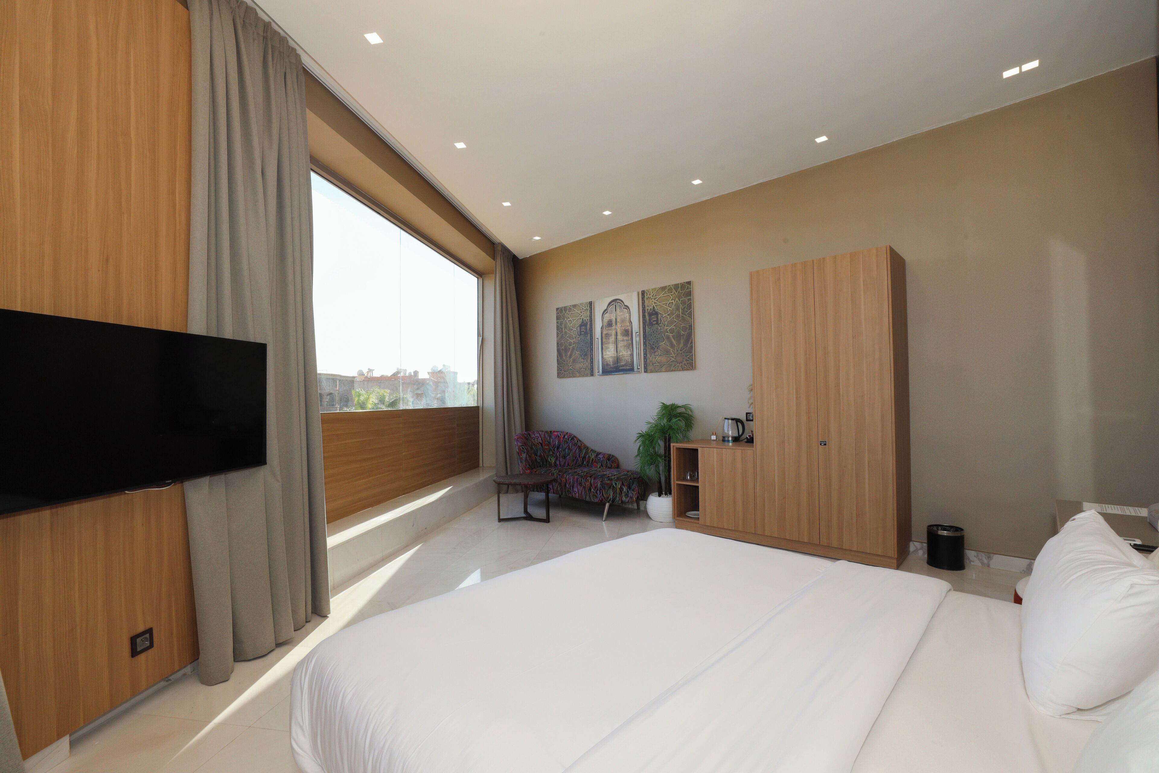 A modern hotel room with a large bed, a flat-screen TV, a sofa, a desk, and a wardrobe.
