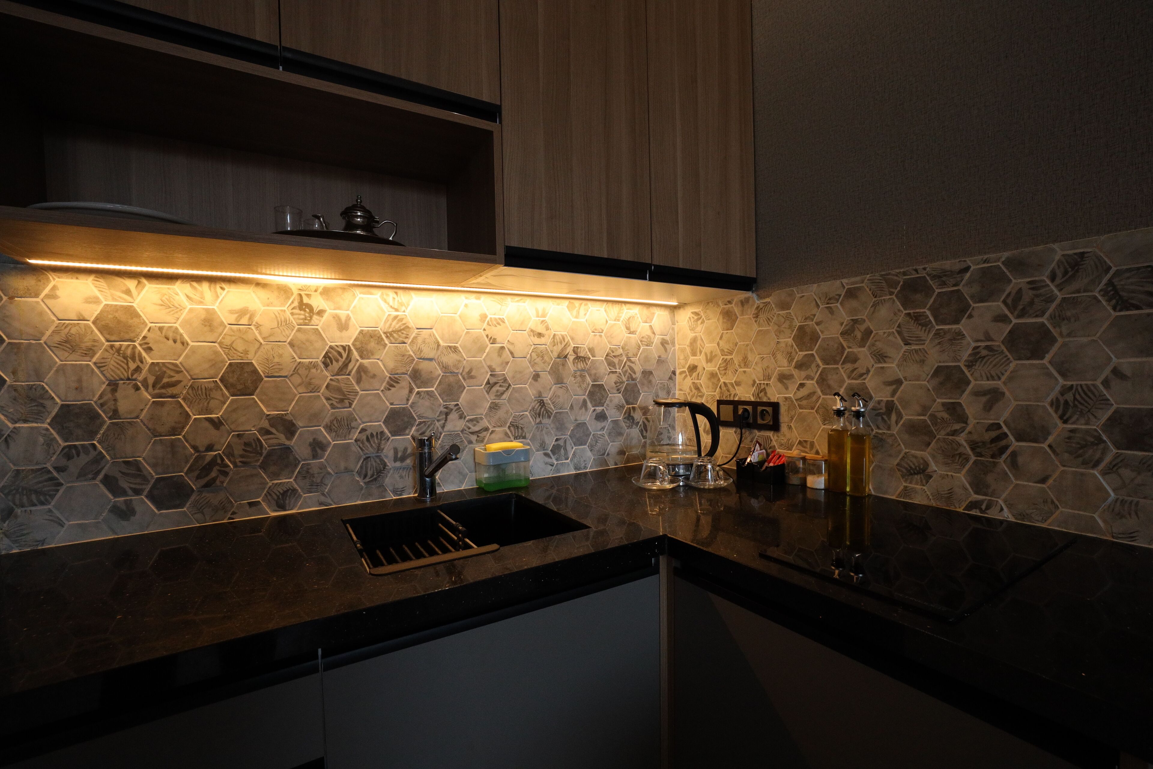 Una cocina moderna con salpicadero de azulejos hexagonales, encimera negra y armarios de madera.