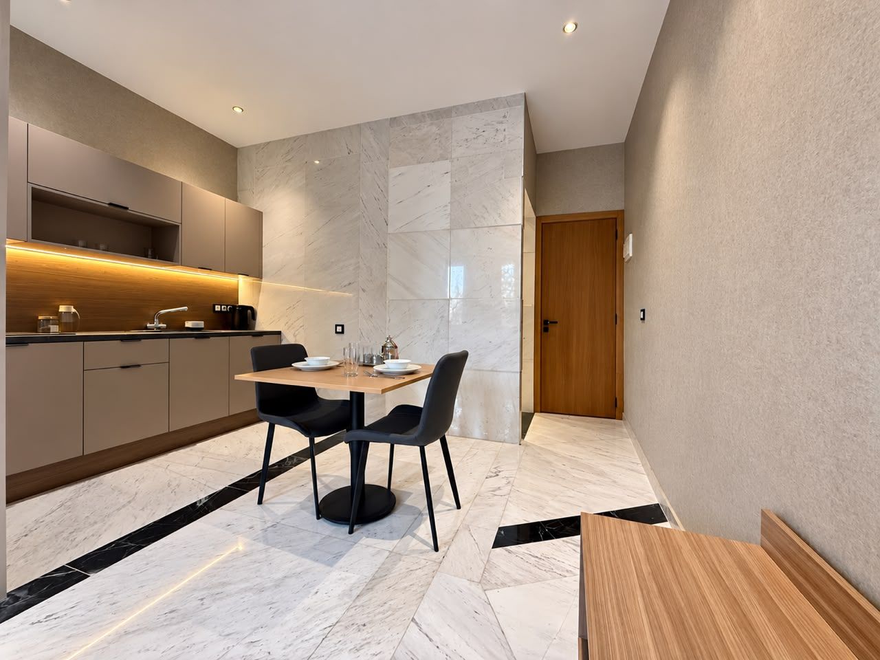 Una cocina moderna con encimeras de mármol, una zona de comedor con mesa y sillas, y una puerta de madera.