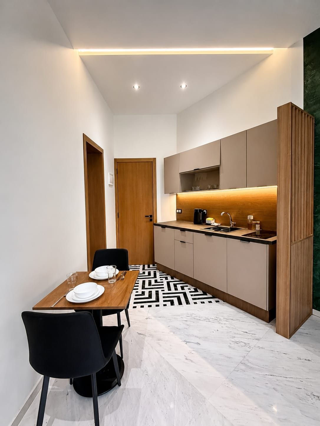 Une cuisine compacte avec un coin repas, comprenant une table en bois, des chaises noires et un sol à motifs.