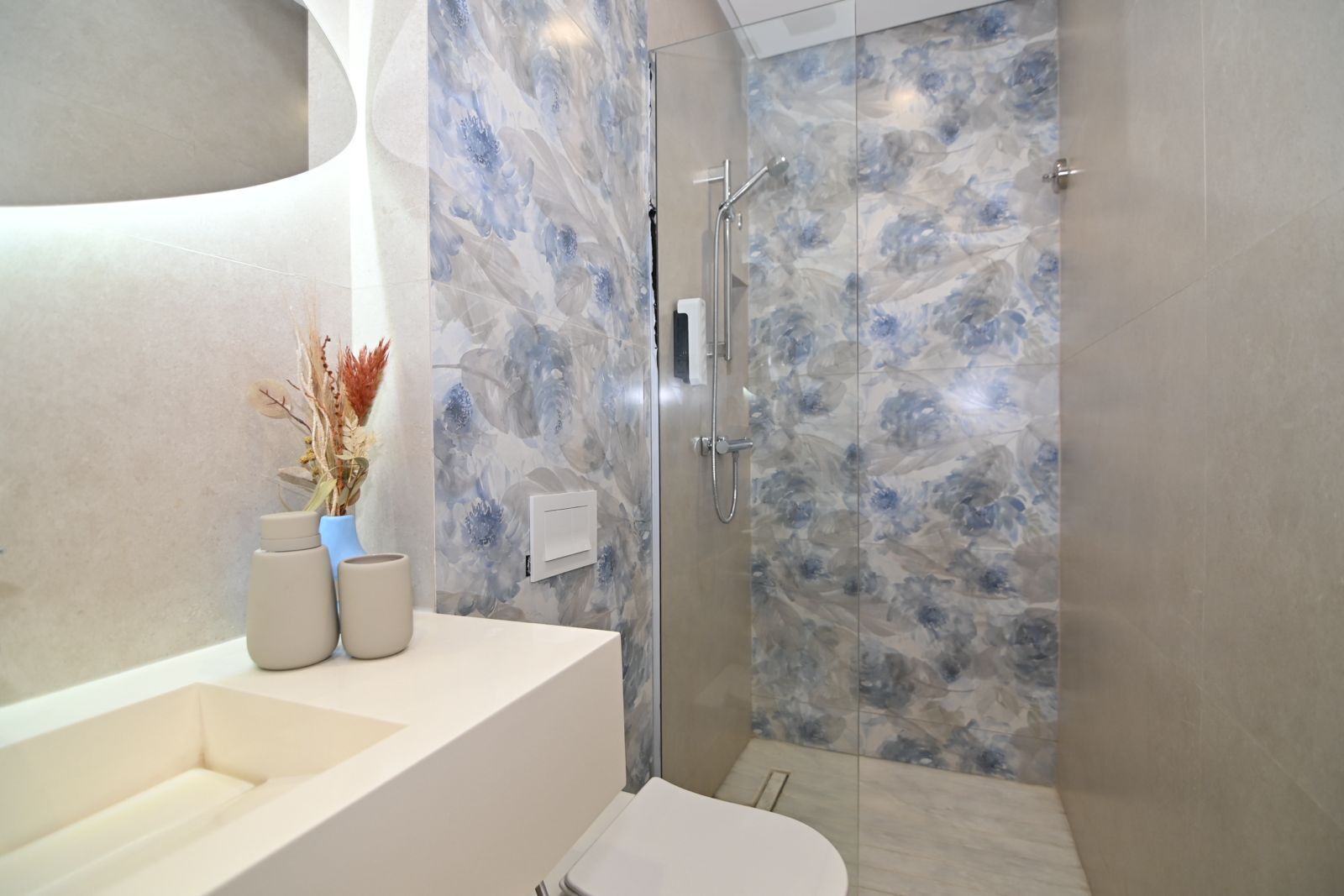 A modern bathroom with a marble shower wall, a white sink, and a vase with dried flowers.