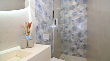 A modern bathroom with a marble shower wall, a white sink, and a vase with dried flowers.