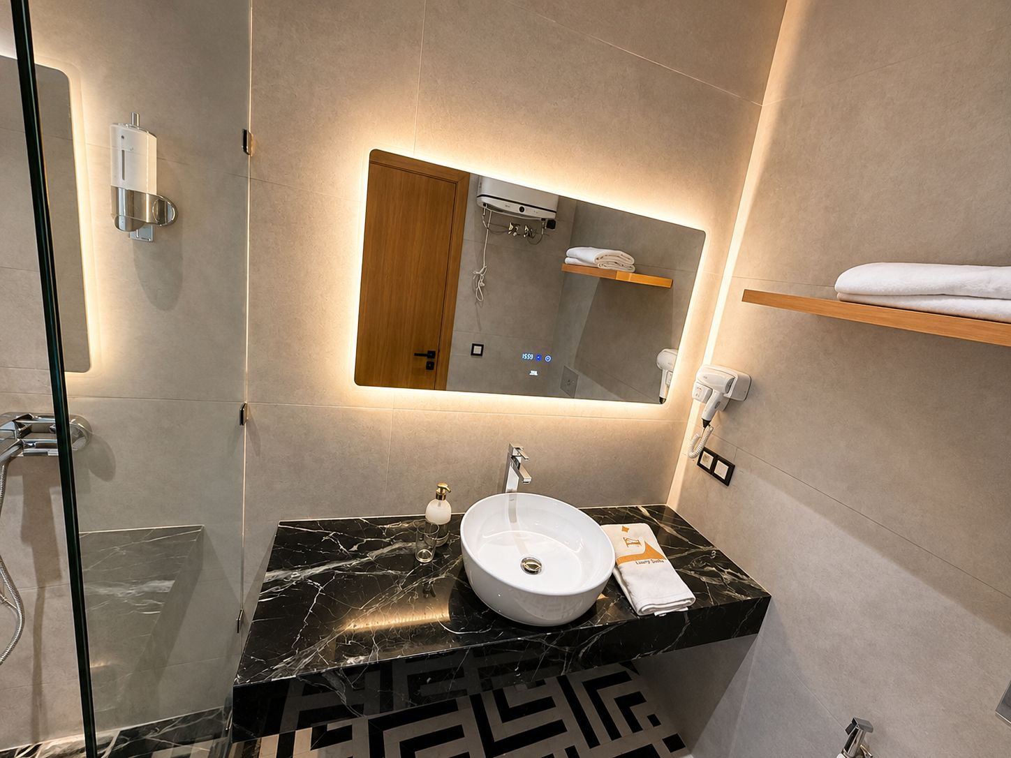 Un baño moderno con lavamanos de mármol, un espejo, un perchero para toallas y una cabina de ducha con paredes de vidrio.
