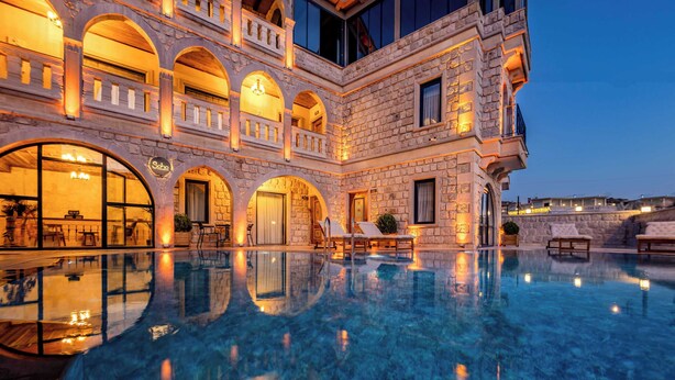 A luxurious pool area with clear water, stone architecture, and outdoor seating. - Soho Cappadocia (Nevşehir)