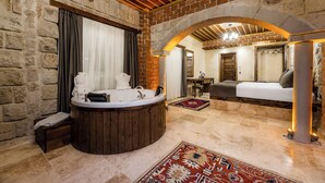 A room with a stone wall, a wooden bathtub, a bed, and a small table. - Soho Cappadocia (Nevşehir)