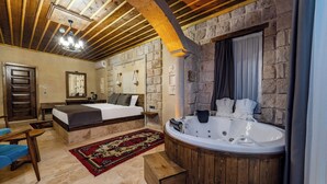 A bedroom with a large bed, a wooden bathtub, a stone wall, and a wooden ceiling. - Soho Cappadocia (Nevşehir)