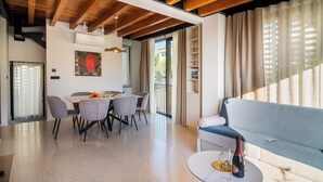 Una sala de estar moderna con techo de madera, una zona de comedor con mesa y sillas, y un sofá con una botella de vino sobre una mesita.