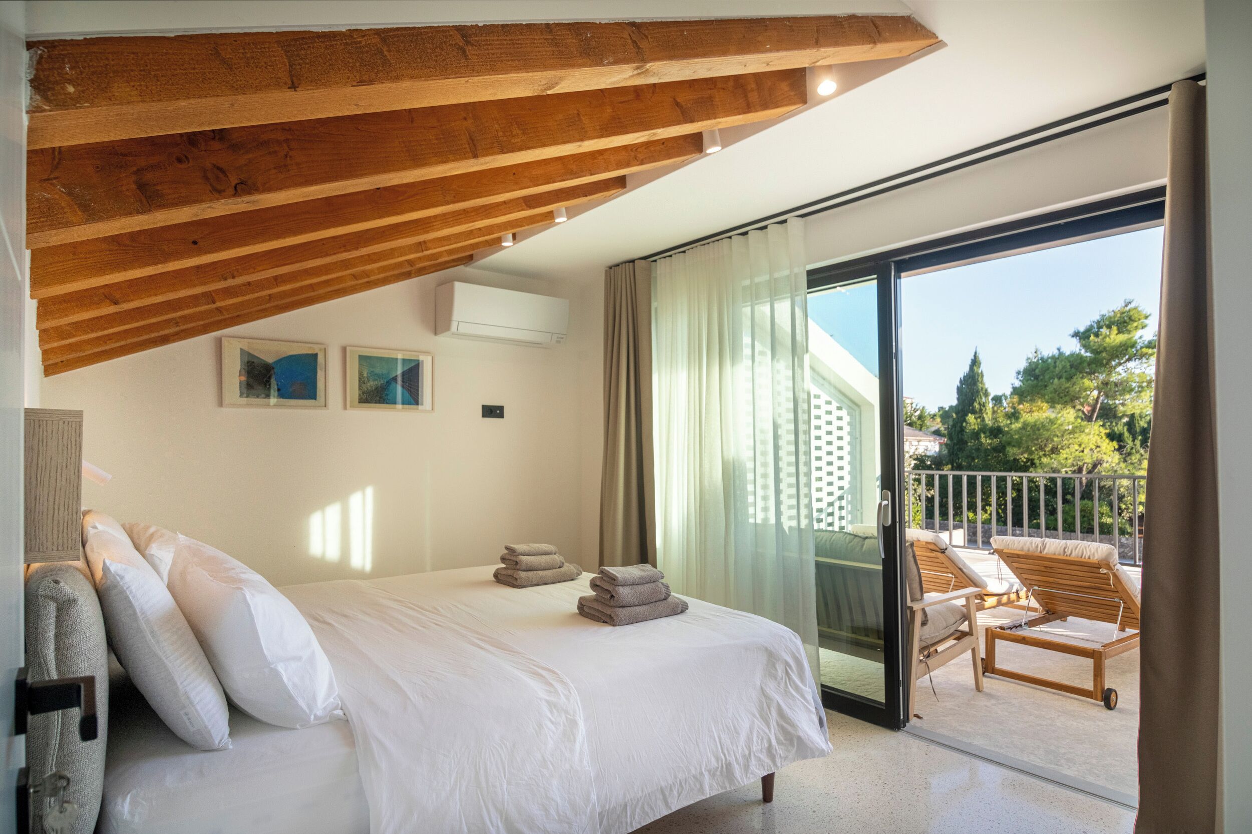 A bedroom with a large bed, a balcony with chairs, and a view of the outdoors.