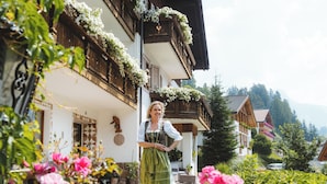 A traditional wooden house with a balcony adorned with flowers, surrounded by lush greenery and vibrant flowers. - Garni Cir (Santa Cristina Val Gardena)