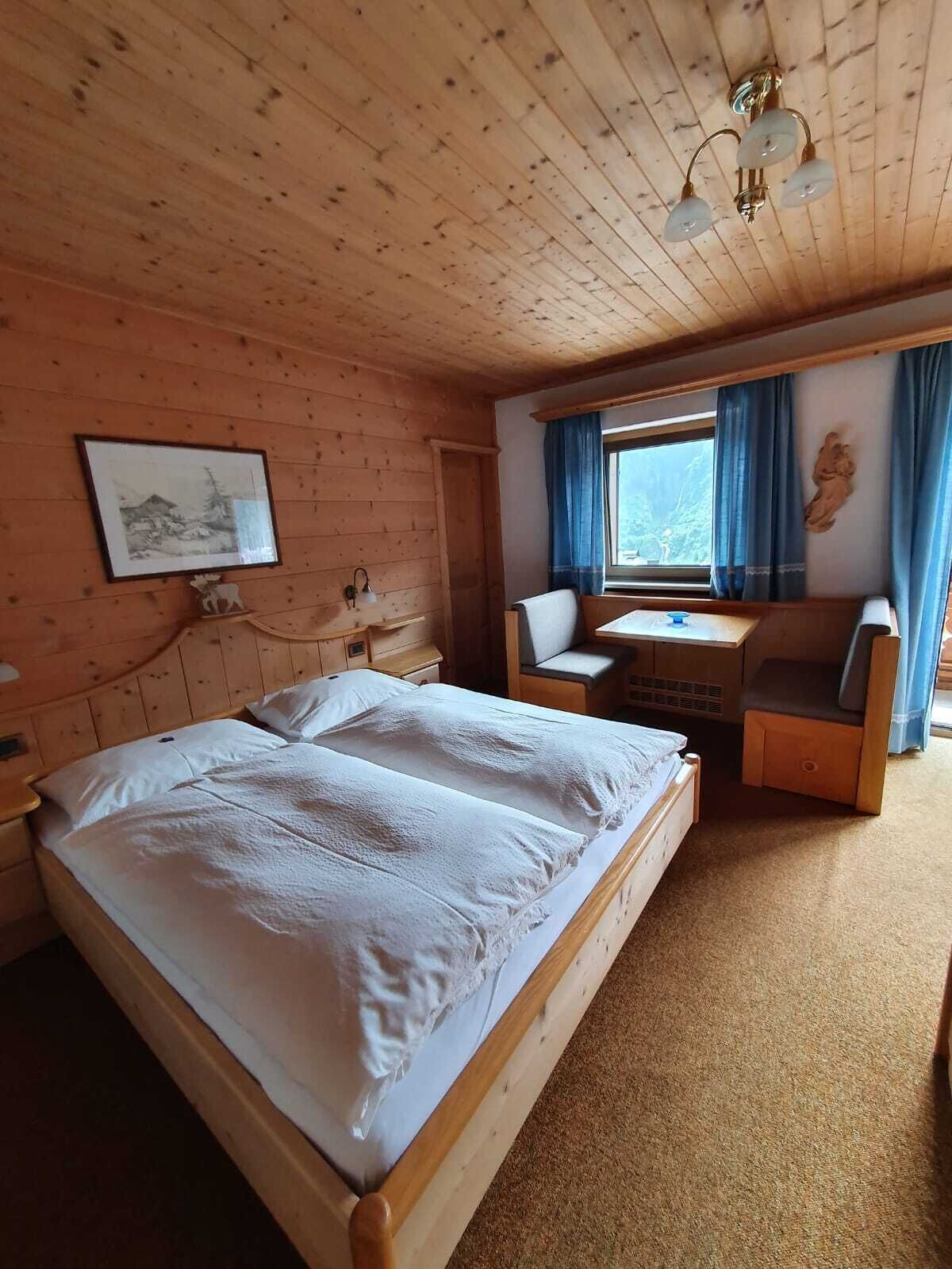 A wooden cabin room with a bed, a desk, and a chair.