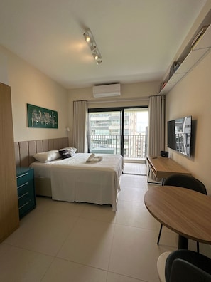 Ein Hotelzimmer mit Bett, Schreibtisch, Stuhl, Fernseher und einem Balkon mit Blick auf Gebäude.