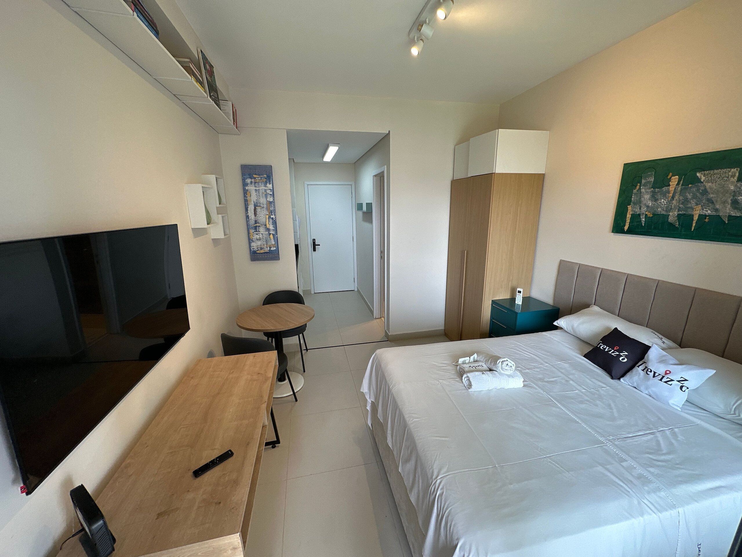 Ett hotellrum med en säng, ett nattduksbord, en tv och ett litet skrivbord.