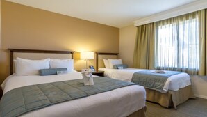 Une chambre d’hôtel avec deux lits, une table de chevet, une lampe et une fenêtre avec des rideaux.