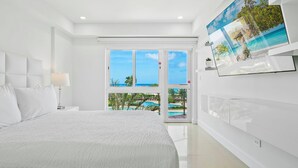 A modern hotel room with a large bed, a TV mounted on the wall, and a view of a pool and beach through the windows. - Oceania 343 J.e. Irausquin Blvd 238 (Oranjestad)