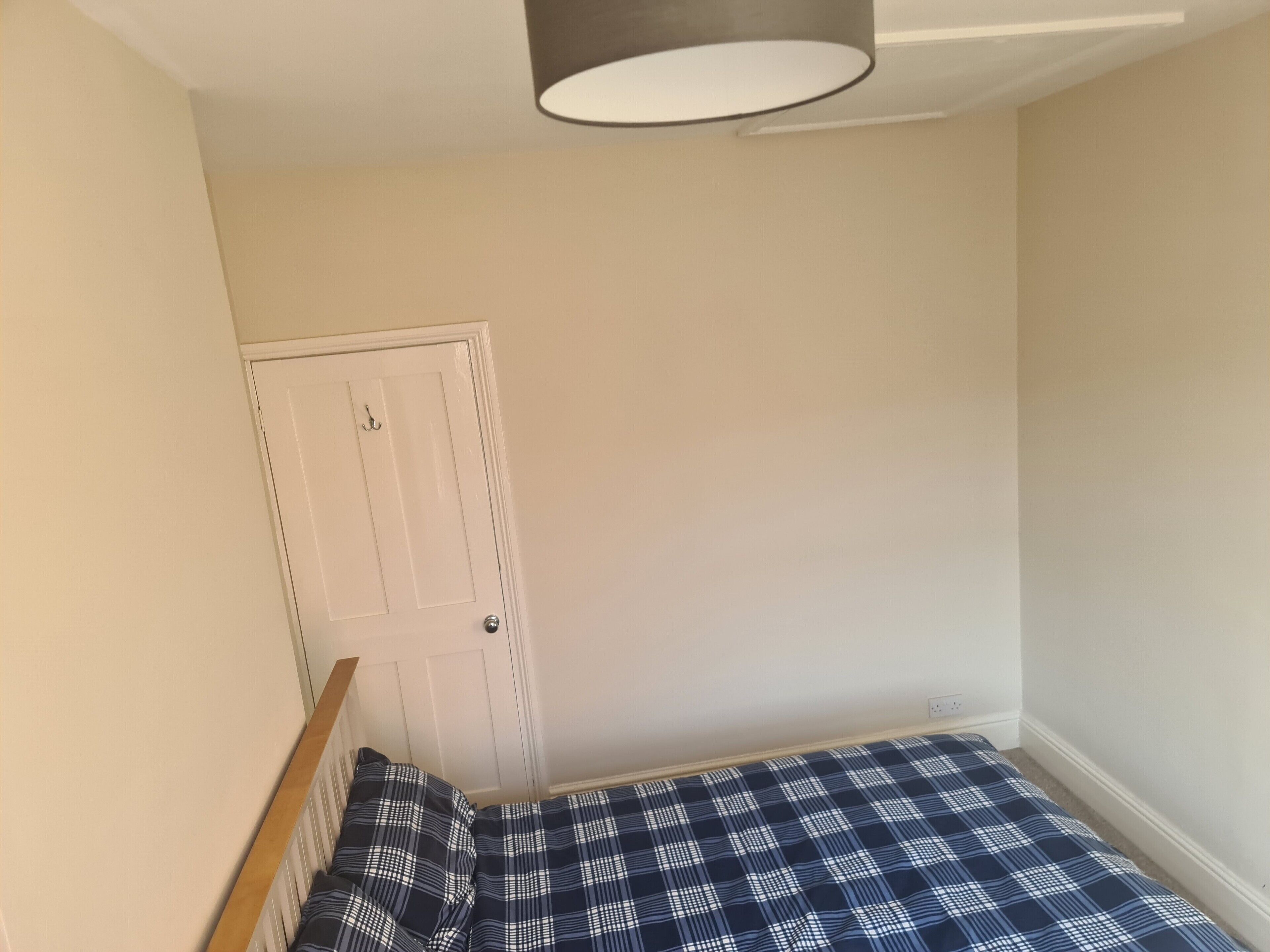 Una piccola camera con un letto singolo, copriletto a scacchi, una porta bianca e un lampadario al soffitto.