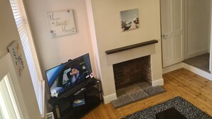 A living room with a fireplace, a clock, a television, and a door. - Quaint 2-bedroom house in Leicester for a cozy getaway (Leicester)