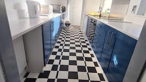 A narrow kitchen with checkered flooring, white countertops, and blue cabinets. - Quaint 2-bedroom house in Leicester for a cozy getaway (Leicester)