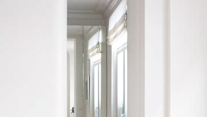 Un pasillo con paredes blancas y suelo de madera que conduce a una habitación con un ventanal y una puerta.