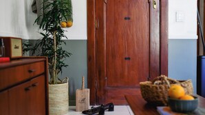 Un gabinete de madera, una cesta trenzada, una planta en maceta, un par de zapatos y un frutero sobre un suelo de baldosas.