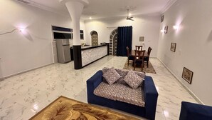 Una sala de estar moderna con un sofá azul, una mesa de centro de madera y una zona de cocina con un refrigerador y una mesa de comedor con sillas.