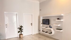 Un interior moderno con una puerta blanca, una planta en maceta, un televisor montado y estanterías empotradas.