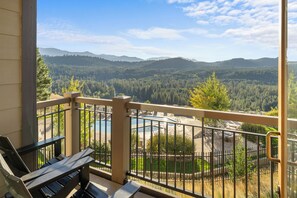 A balcony with a view of a forested valley and a swimming pool.