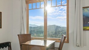 A room with a large window offering a mountain view, a wooden table, and two wicker chairs. - Tranquil Suncadia Lodge with Fireplace, Mountain Views and Pool Hot Tub (Cle Elum)