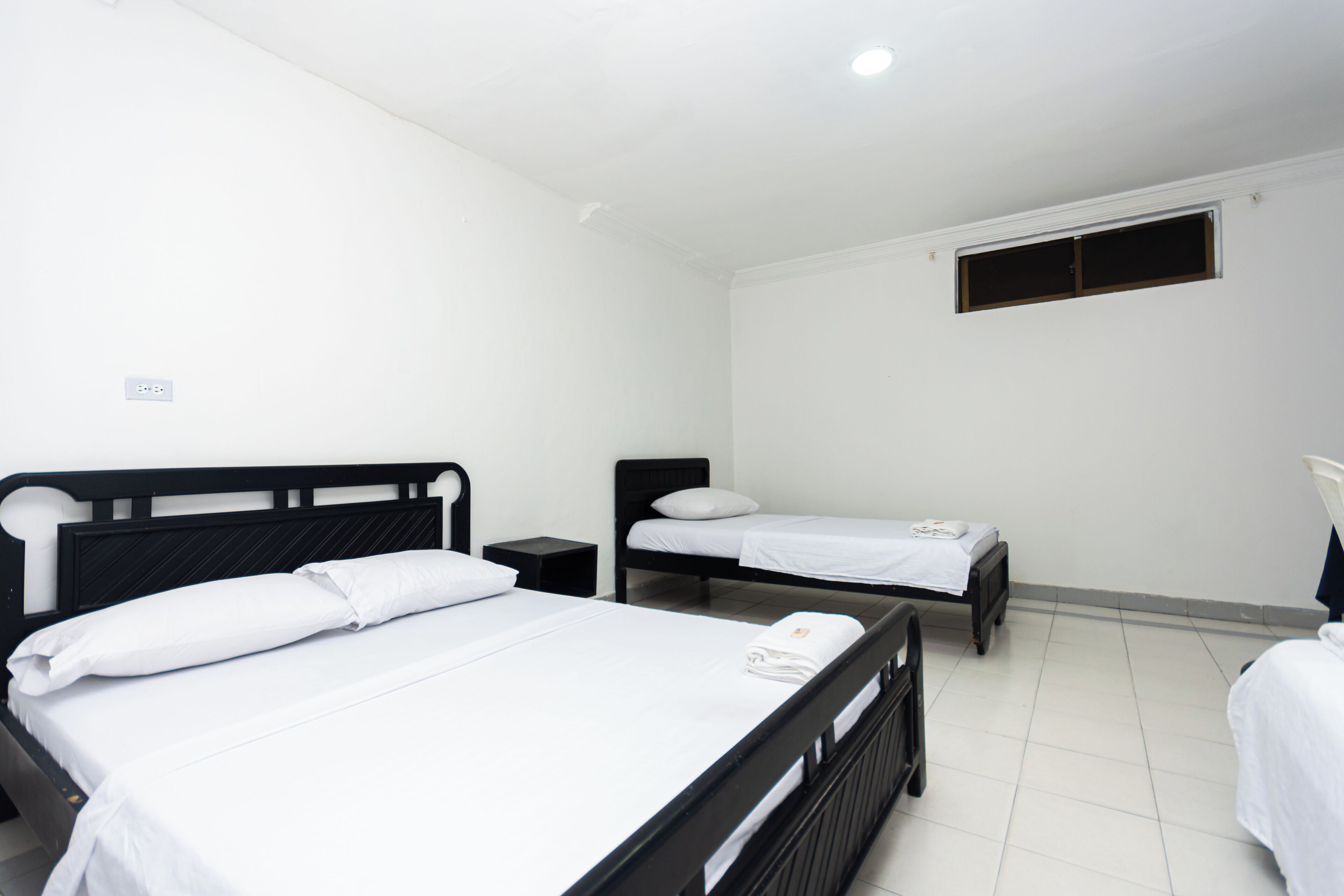 Una habitación con dos camas individuales, una mesita de noche pequeña y una ventana con persianas cerradas.