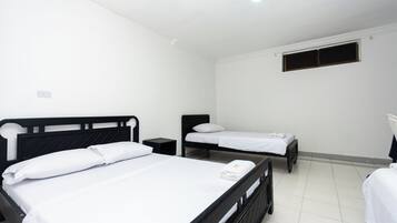 Una habitación con dos camas individuales, una mesita de noche pequeña y una ventana con persianas cerradas.