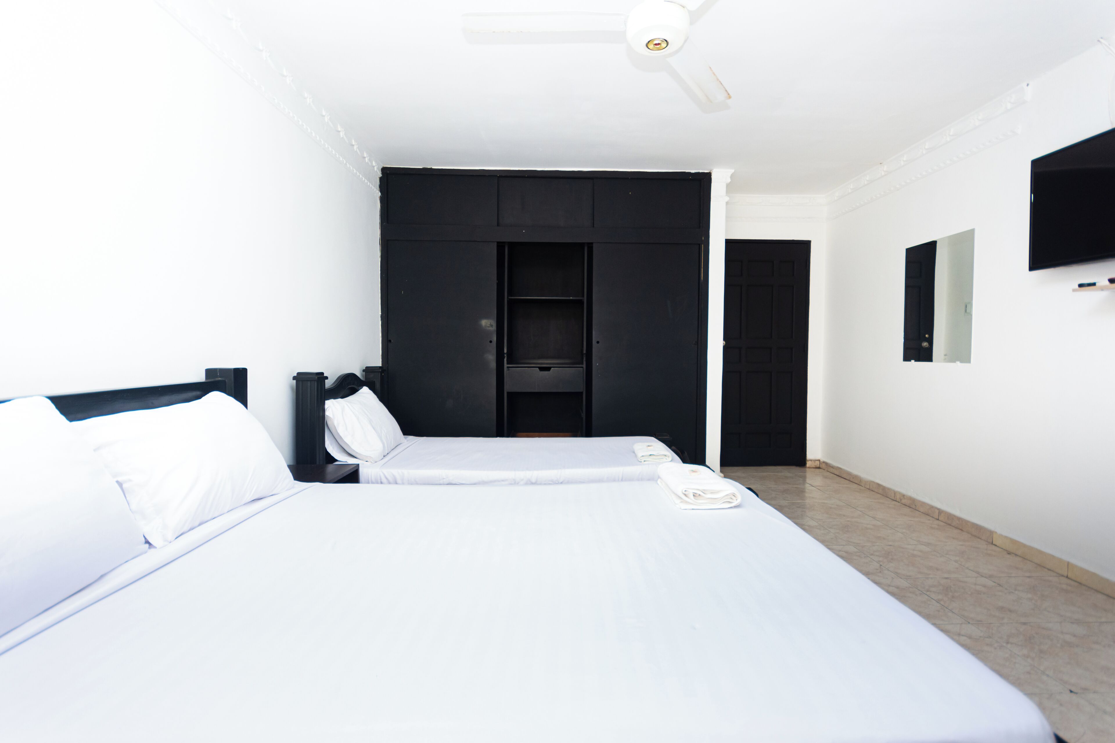 A hotel room with a large bed, a wardrobe, a television mounted on the wall, and a door leading to another room.