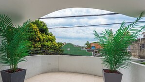 A balcony with two potted plants, a tiled floor, and a view of a green building and a blue sky. - COSTA CARIBE BAQ HOTEL (Barranquilla)