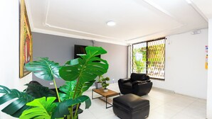 A living room with a black leather sofa, a coffee table, and large green plants. - COSTA CARIBE BAQ HOTEL (Barranquilla)