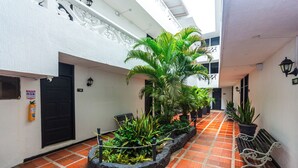A corridor with a tiled floor, potted plants, a bench, and a door with a fire extinguisher. - COSTA CARIBE BAQ HOTEL (Barranquilla)
