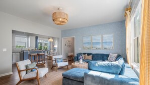 Ein modernes Wohnzimmer mit einem blauen Sofa, Holzstühlen, einer Küchenzeile und einem Esstisch.