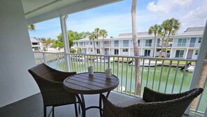 Ein Balkon mit Korbstühlen und einem Tisch, der auf einen Yachthafen mit Booten und einem Gebäude mit weißer Fassade blickt.