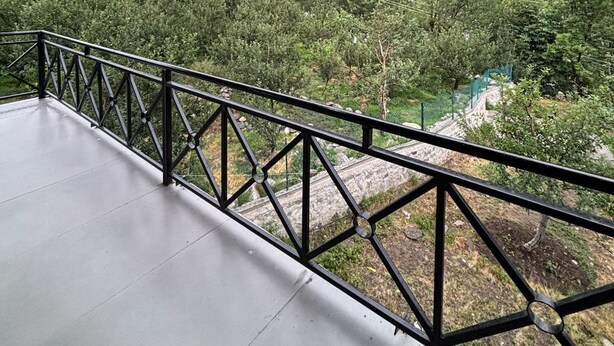 A balcony with a metal railing overlooking a mountainous landscape with dense forests and a river. - Holidays in Haven Hospitality  (Manali)