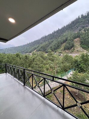 A balcony with a metal railing overlooking a mountainous landscape with dense forests and a river. - Holidays in Haven Hospitality  (Manali)
