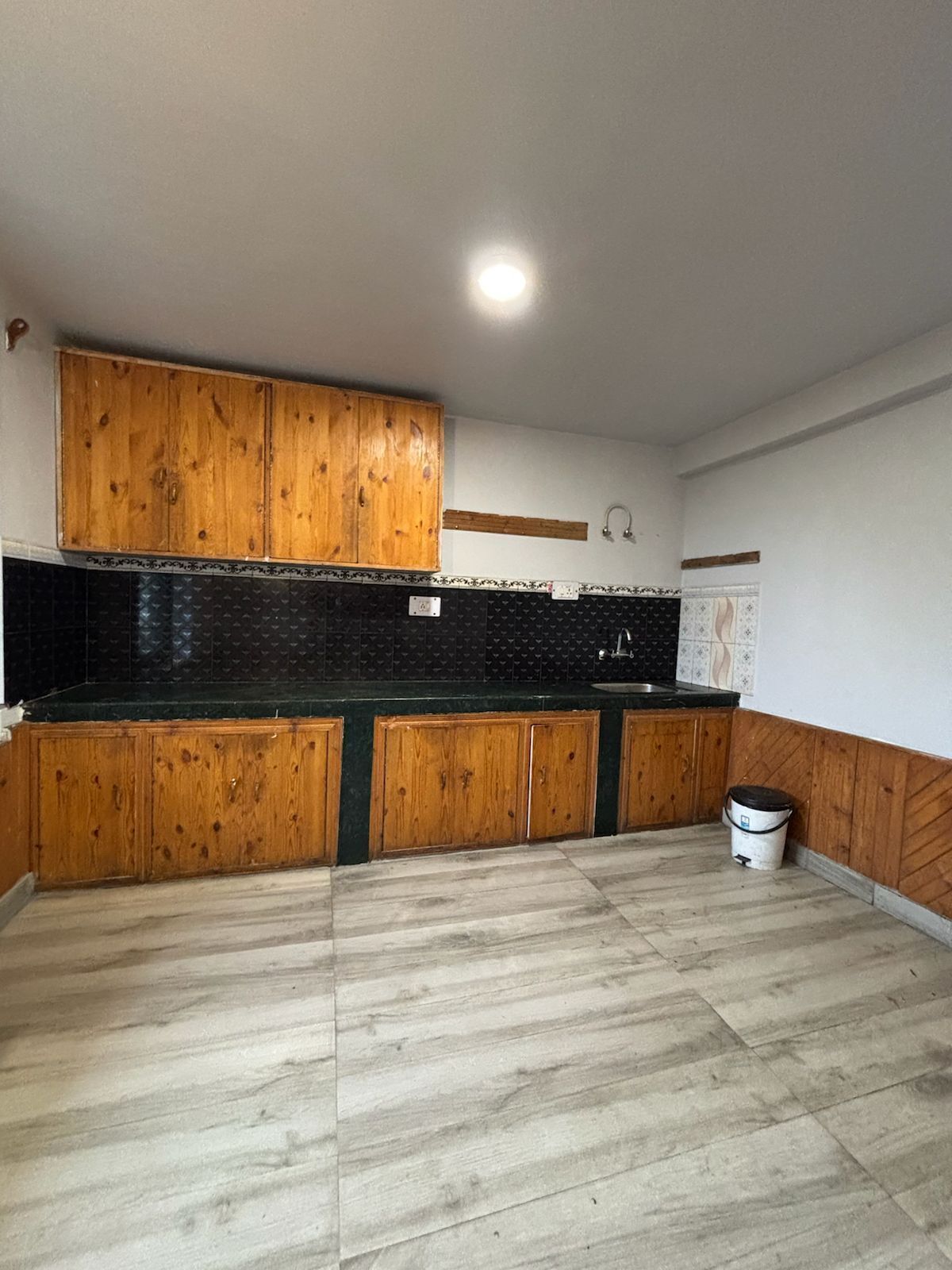 A kitchen with wooden cabinets, a black backsplash, and a light-colored floor.