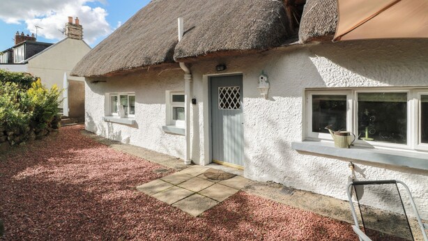 A traditional thatched-roof cottage with a white exterior, a small front porch, and a gravel driveway. - Rowantree Cottage (Kelso)
