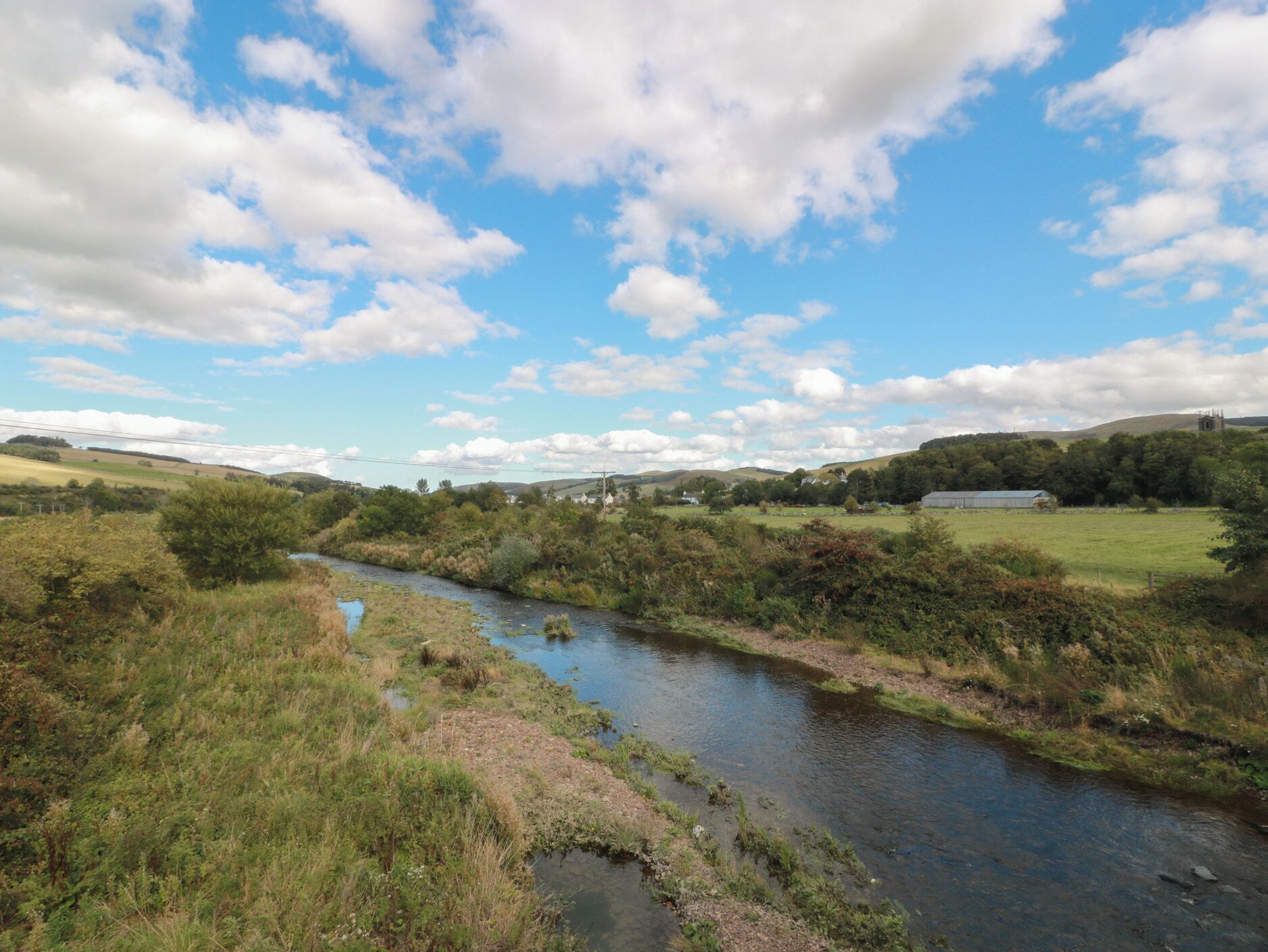 Un río serpentea por un paisaje rural con campos y una iglesia a lo lejos.
