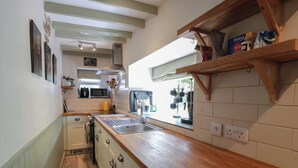 A narrow kitchen with wooden countertops, a built-in microwave, and a window with hanging pots. - Rowantree Cottage (Kelso)