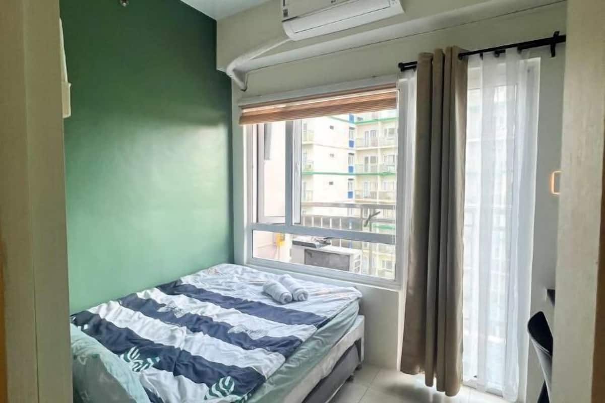 Une chambre à coucher avec un lit, une fenêtre avec des rideaux et une vue sur les bâtiments à l’extérieur.