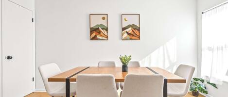 Un comedor con una mesa de madera, seis sillas y dos cuadros en la pared.