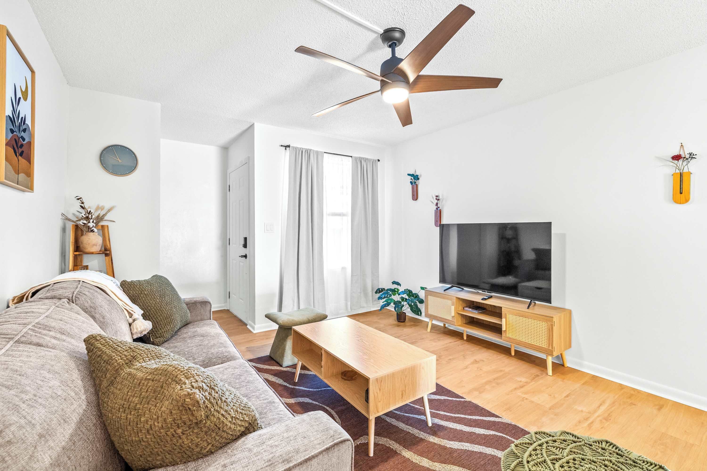 Ein modernes Wohnzimmer mit Sofa, Couchtisch, Fernseher und Deckenventilator.