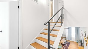 A staircase with wooden steps and metal railings, leading to a room with a wooden floor, a small table, and a TV. - The Capri Villa Stay for 6 (Tampa)