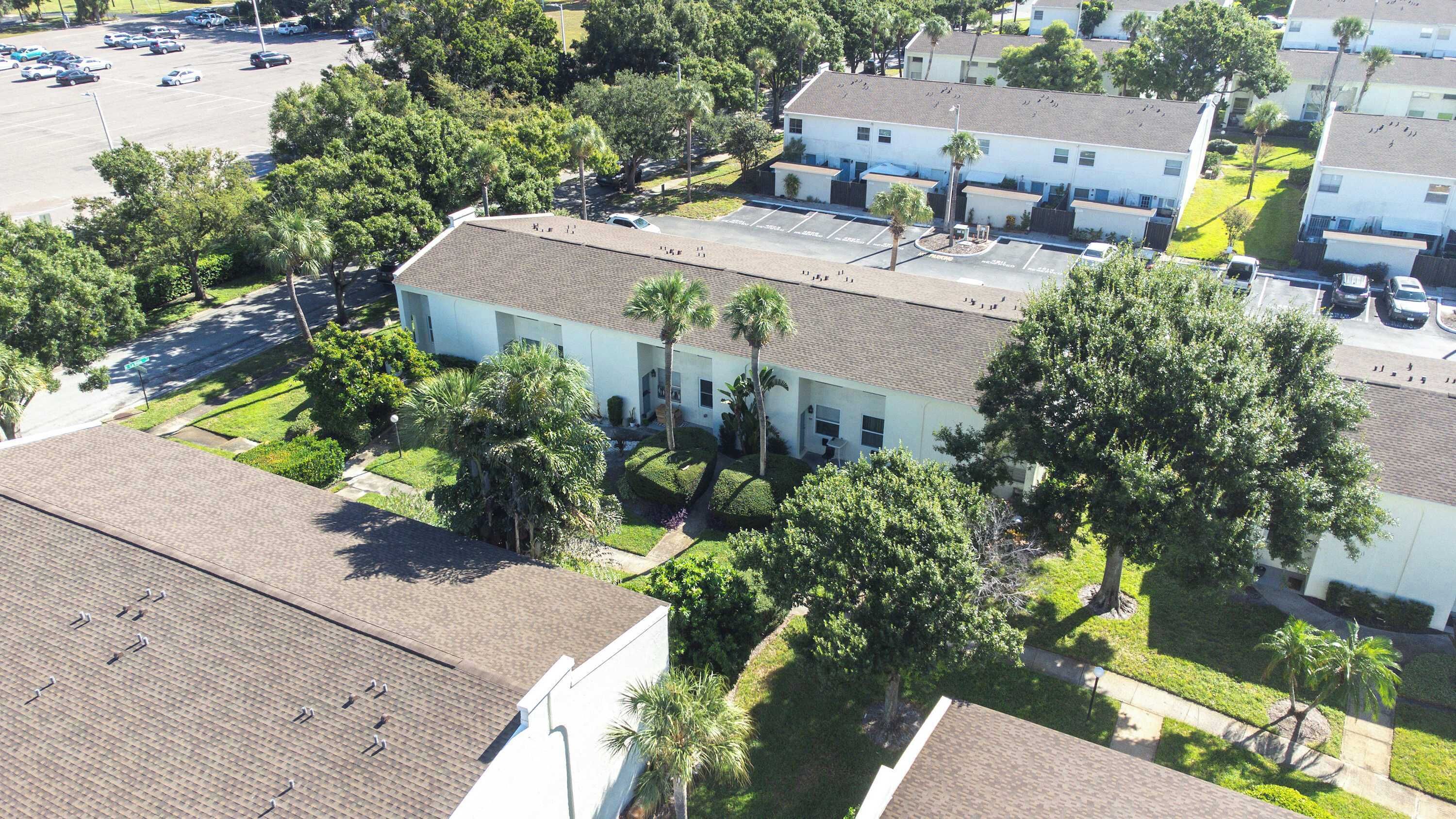 Vista aérea de una zona residencial con un edificio blanco de techo plano, rodeado de abundante vegetación y palmeras.