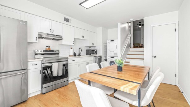 A modern kitchen with white cabinets, stainless steel appliances, and a wooden dining table with white chairs. - The Capri Villa Stay for 6 (Tampa)