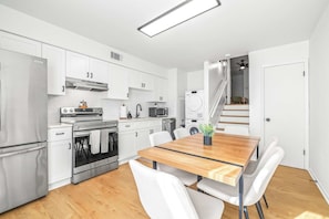 A modern kitchen with white cabinets, stainless steel appliances, and a wooden dining table with chairs. - The Capri Villa Stay for 6 (Tampa)