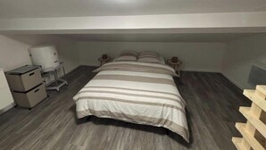 Habitació petita i poc il·luminada, amb un llit individual, una tauleta de nit, una taula petita i un radiador.