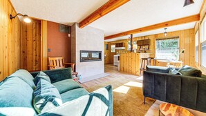 Ein gemütliches Cabin-Interieur mit Wohnbereich, inklusive einer Couch und einem dunklen Sessel, einer Küche mit Holzausbau und einem großen Fenster mit Blick ins Freie.